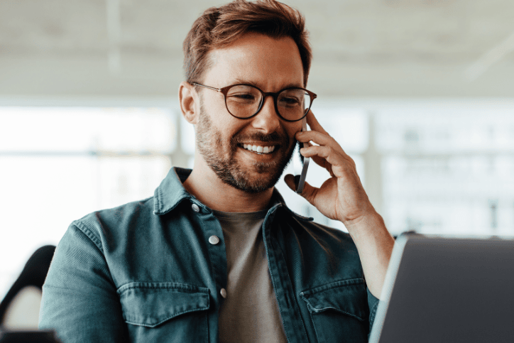 man in front of laptop speaks on phone